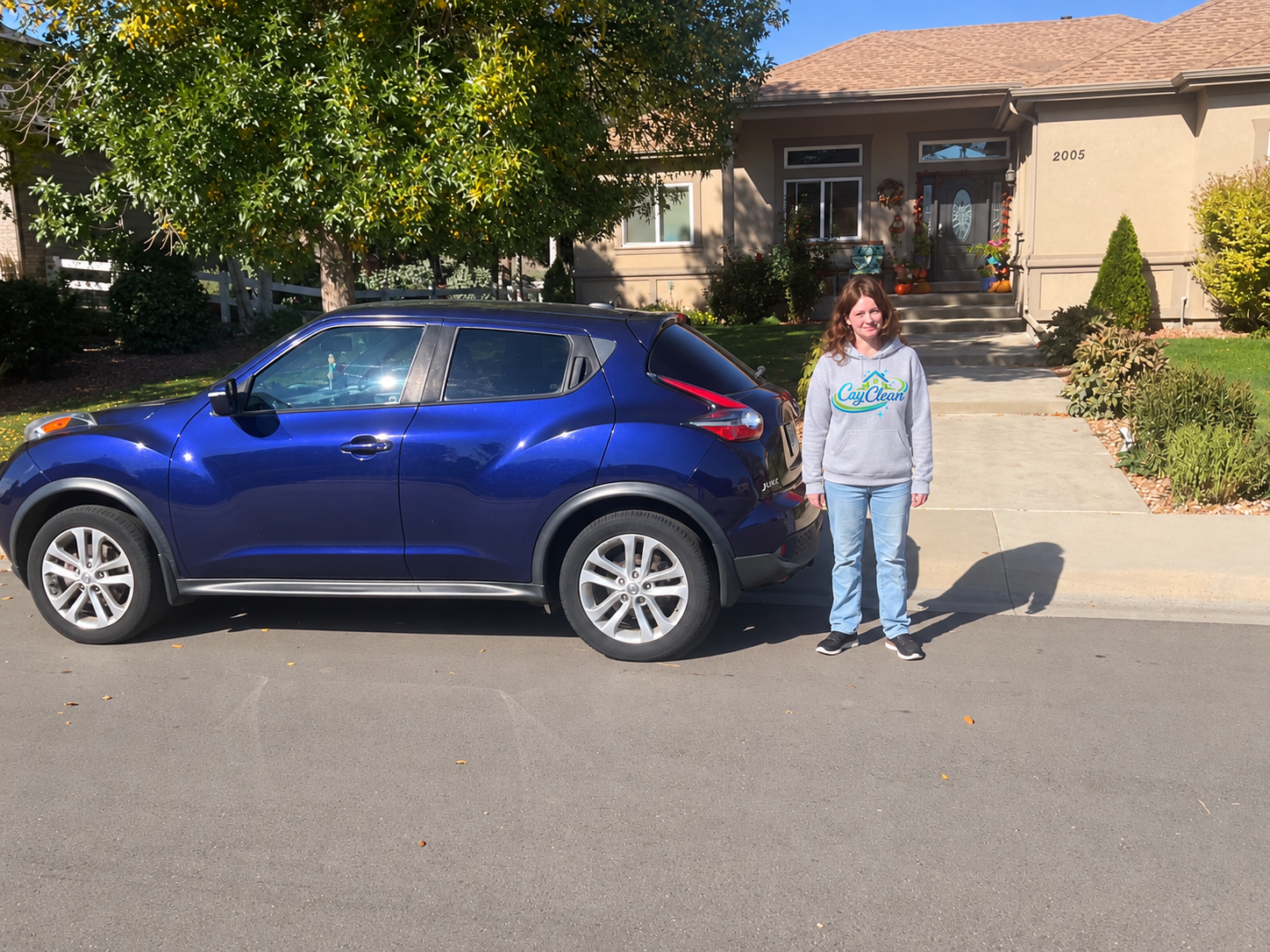 Caylee of CayClean standing beside her blue vehicle outside a home